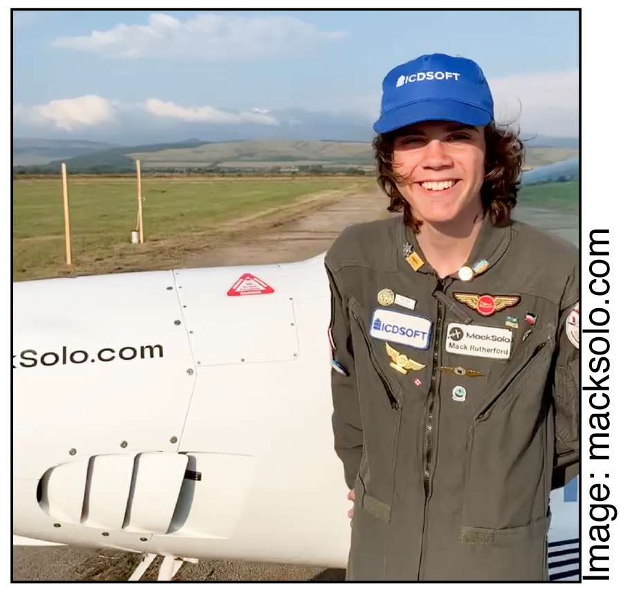 Mac Solo wearing a baseball cap in pilot uniform standing in front of a plane.
